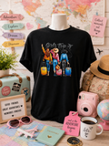 Custom Graphic T-Shirt- featuring a design of three girls traveling, each with her own suitcase.